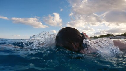 Wall Mural - Boy swims at sunset in open ocean with cloudy sky