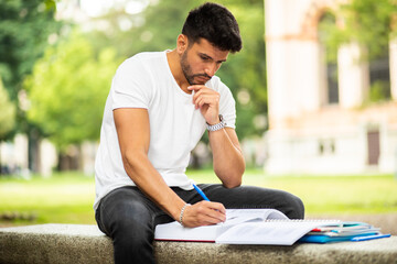 Handsome young man reading book on bench in the park