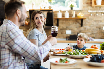 Wall Mural - Happy young couple toasting with red wine while having a lunch at home