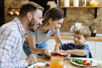 Wall Mural - Happy mother serving food to her family while father and son having fun in dining room