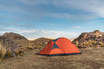 orange colored camp in the mountains in a sunset surrounded by rocks and yellow vegetation in the wi