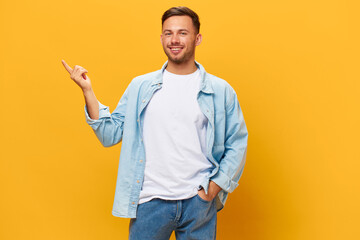 Wall Mural - Happy cheerful tanned handsome man in blue basic t-shirt point finger aside look at camera posing isolated on yellow studio background. Copy space Banner Mockup. People emotions Lifestyle concept