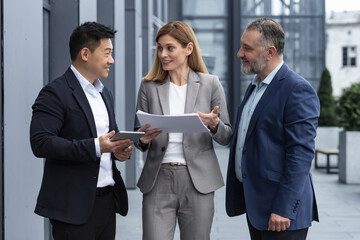 Three businessmen outside office building with documents discussing plans, businessmen and businesswoman having fun chatting and talking, diverse business group in business suits