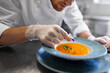 © Syda Productions - food cooking, profession and people concept - close up of male chef with flower serving plate of pumpkin cream soup at restaurant kitchen