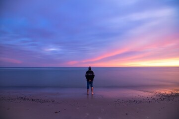 Canvas Print - Back shot of an adult man stands at the beach looking at the sea and dusk sky