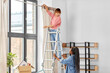 Leinwandbild Motiv moving, home improvement and real estate concept - happy smiling women with ladder hanging curtain