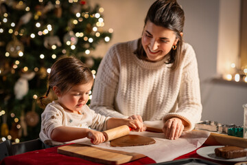 Poster - family, cooking and winter holidays concept - happy mother and baby daughter with rolling pin making gingerbread cookies from dough at home on christmas