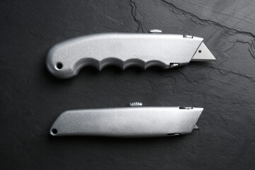 Canvas Print - Two utility knives on black table, flat lay