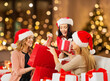 © Syda Productions - christmas, holidays and people concept - smiling women in santa hats with shopping bags and many gift boxes over festive lights on background