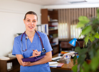 Wall Mural - Portrait of friendly female doctor wearing uniform standing in modern clinic