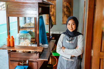 veiled woman wearing apron smiling with arms crossed while standing at the stall beside the door