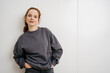 © contrastwerkstatt - young redhead woman in front of a white wall and looks thoughtfully into the camera