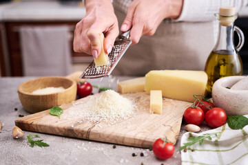 Wall Mural - Woman grates Parmesan cheese on a wooden cutting board at domestic kitchen