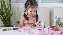 Asian adorable funny little girl making makeup dips brush into bottle to paints nails polish red nail varnish herself, Learning activity to be woman, happy kid is beautiful make up with cosmetics toy