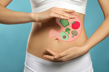 Wall Mural - Woman with image of stomach full of food drawn on her belly against light blue background, closeup. Healthy eating habits