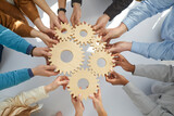 Fototapeta  - Business people or office workers hold wooden gears that symbolize well-coordinated teamwork. Top view close up of hands of multiracial men and women standing in circle. Concept business cooperation