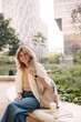 Smiling young caucasian woman looking at camera enjoying weather sitting outdoors. Blonde female student wears casual clothes and backpack. Rest time concept