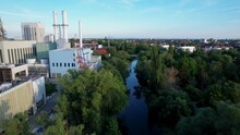 Large Gas-fired Power Station In The German City Of Braunschweig On The Calm River Oker With A Clear Blue Sky In The Background. Fast Forward Drone Dolley Shot