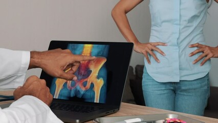 Wall Mural - Doctor showing x-ray of pain in the hips on a laptop with woman patient