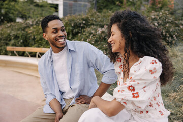 Wall Mural - Cheerful african young couple are relaxing outdoors enjoying each other. Brunette girl and guy are wearing shirt with blouse. Happy day concept