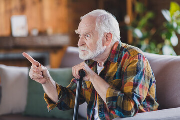 Poster - Photo of nervous angry retired man dressed plaid shirt holding nursery cane pointing finger sitting couch indoors apartment