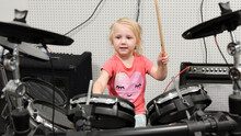 A Little Girl Tries To Play The Drum Kit At A Music School.