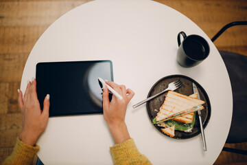 Beautiful young woman using digital tablet with digital pencil at cafe table with cup of coffee. Overhead top view.