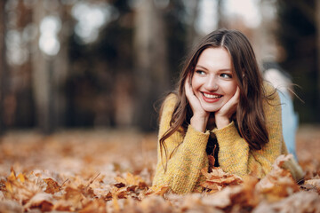 young woman model lying in autumn park with yellow foliage maple leaves. fall season fashion