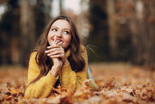 Young Woman Model Lying In Autumn Park With Yellow Foliage Maple Leaves. Fall Season Fashion