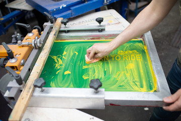 Serigraphy silk screen print process at clothes factory. Cleansing Frame, squeegee and plastisol color paints.