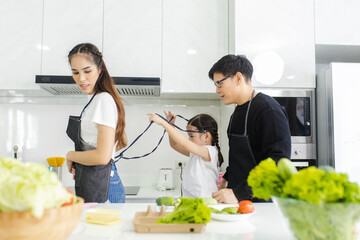 Asian family couple, husband and child help his to put on apron before cooking in the kitchen at home,  happy father and son concept.