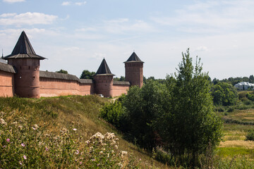 Brick walls of the ancient Kremlin in Suzdal russia on a high hill among green trees and grass on a bright sunny summer day and a space for copying