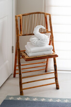 White Guest Bath Towel Folded In Fancy Style In Shape Of Swan Sitting Atop Stack Of Towels On Chair In Bed And Breakfast Hotel Bathroom