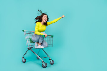 Wall Mural - Full size photo of overjoyed carefree girl sit inside market trolley ride empty space isolated on teal color background