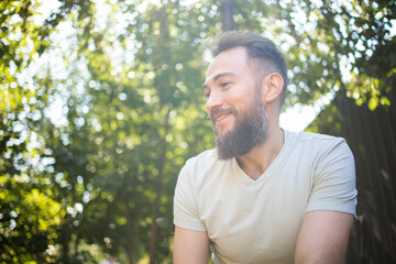 portrait of middle aged handsome bearded man dreaming in sunlight in summer park.