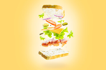 On a yellow background, a sandwich with pieces of meat, vegetables, cheese, herbs in a frozen flight. Creative composition. Minimalism. There are no people in the photo.