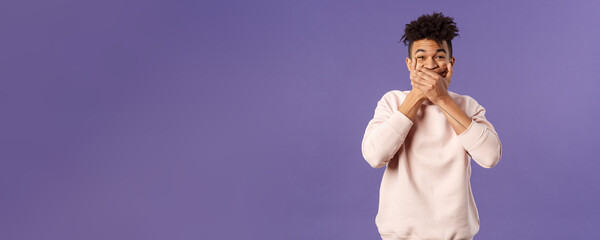 Portrait of amused, funny and carefree male student fooling around during class lecture, giggle, trying not laugh out loud so shut his mouth with hands, chuckle over hilarious joke