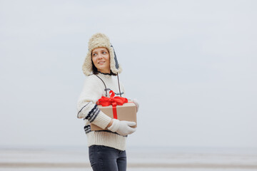 woman in a Santa Claus hat with a gift box in her hands smiles. a happy European woman carries a gift for New Year or Christmas. give gifts and surprises, poster postcard. holiday holidays Christmas