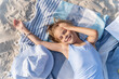 © Cavan Images - A girl on the beach is resting on a towel and smiling.