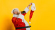 Drunk Santa. Fat santa claus drinks champagne from the neck of a bottle and holds a cap in his hand on a yellow isolated background with copy space.