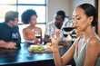 © Kirsten D/peopleimages.com - A woman drinking a glass of wine at a dinner table with friends in a restaurant and enjoying the luxury alcohol. Young African American female having fun dining with people at a celebration