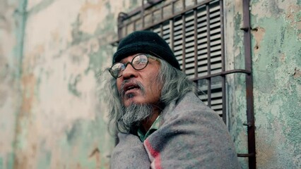 Wall Mural - 4k, An old Asian man with long hair wrapped in an old wall, a homeless man who waits for help from others, food and money, because he has no work to do and has to sleep on the streets all night.