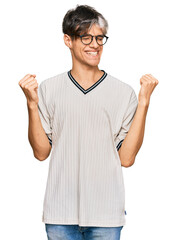 Canvas Print - Young hispanic man wearing casual clothes and glasses very happy and excited doing winner gesture with arms raised, smiling and screaming for success. celebration concept.