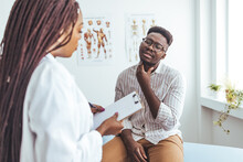 Doctor Listens To The Patient's Complaints While The Patient Points To The Throat. A Doctor Listens To A Man Patient Describe Throat Pain. Young Man Have Problem With Sore Throat Or Thyroid Gland.