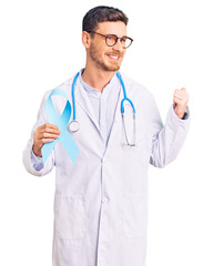 Handsome young man with bear wearing doctor uniform and holding blue ribbon pointing thumb up to the side smiling happy with open mouth