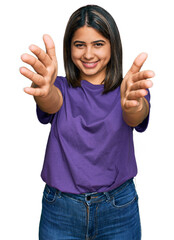 Sticker - Young hispanic girl wearing casual purple t shirt looking at the camera smiling with open arms for hug. cheerful expression embracing happiness.