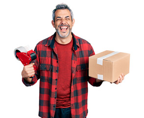 Canvas Print - Middle age hispanic with grey hair holding packing tape and cardboard box smiling and laughing hard out loud because funny crazy joke.