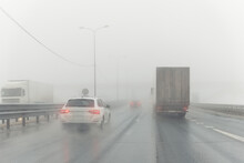 Driver POV On Traffic On Blue Foggy Misty Rainy Slush Highway Intercity Road With Low Poor Visibility On Cold Winter Autumn Morning. Seasonal Bad Rainy Weather Accident Danger Warning. Car Fog Light