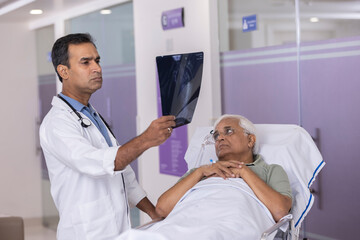 Male doctor examining x-ray report of patient lying on stretcher bed at hospital
