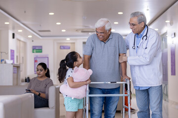 Granddaughter with male doctor teaching disabled grandfather to use walker at hospital
